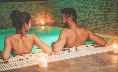 Happy couple enjoying spa swimming pool with candles and soft lights - Young people doing romantic...