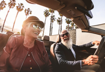 Senior trendy couple inside a convertible car on holiday time - Mature rich people having fun doing a road trip during vacation - Travel, fashion and joyful elderly concept - Main focus on - obrazy, fototapety, plakaty