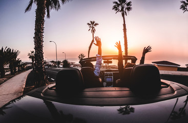 Happy people having fun in convertible car in summer vacation at sunset - Young couple enjoyng ...