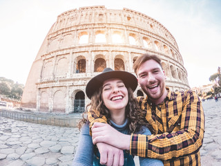 Young couple taking photos with coliseum in background - Happy people having fun with new technology trends traveling europe - Love and tech concept - Soft focus on girl face