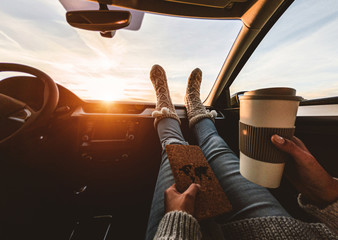 Woman drinking coffee paper cup inside car with feet warm socks on dashboard - Girl relaxing in...