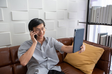 Senior Asian man playing tablet and video call on sofa in living room at home  Portrait of Asian elderly man is Relaxing and Happiness With playing tablet