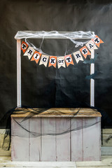 Wooden stand or stall with artificial web and garland with trick or treat inscription on a black background.  Halloween concept.