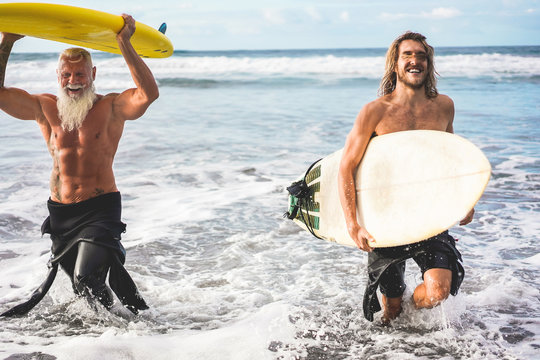 Multigeneration friends going to surf on tropical beach - Family people having fun doing extreme sport - Joyful elderly and healthy lifestyle concept - Main focus on senior face - Powered by Adobe