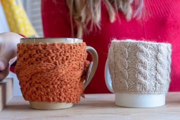 Girl is holding tray with cups in knitted cover with hot drinks.
