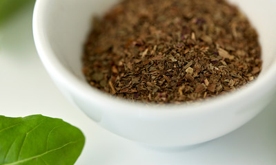 culinary and flavoring concept - close up of dry basil seasoning in white cup
