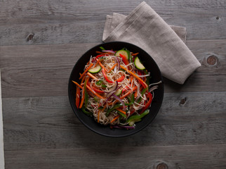 Ensalada de fideos y verdura  sobre bol negro. Noodle and vegetable salad on black bowl.