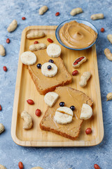 Obraz na płótnie Canvas Funny bear and monkey face sandwich with peanut butter, banana and black currant,peanuts on grey concrete background,top view