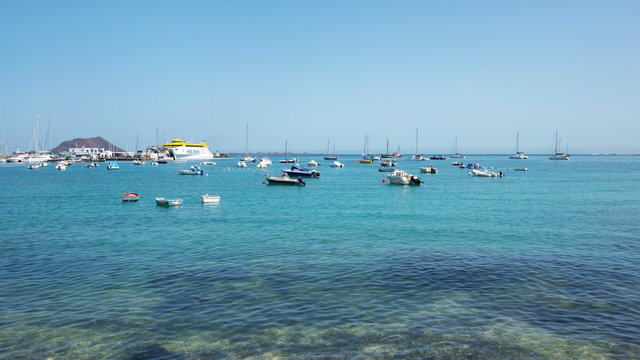 Panoramic views of the harbor with lots of different stationary boats, ferries and yachts and the distant islet of Los Lobos, in Puerto de Corralejo, Fuertentura, Canary Islands, Spain
