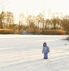Fototapeta na wymiar little lonely boy in winter on ice in the snow