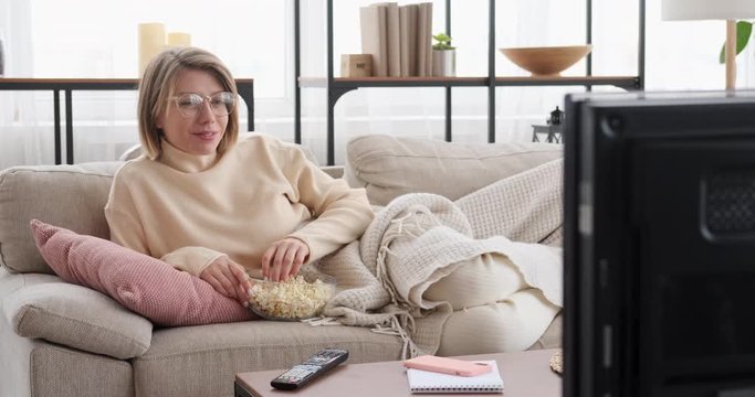 Happy woman eating popcorn while enjoying movie on tv at home