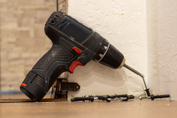 A black home electric screwdriver leaned against the wall. There are screws next to the...