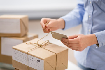 delivery, mail service, people and shipment concept - close up of woman packing parcel box and tying tag by rope at post office