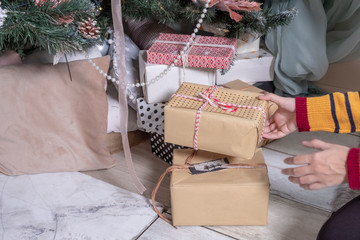 Close up of woman hands putting down a gift box under a Christmas tree.