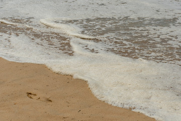 Foam in the waves and lonely footprint on a sandy beach