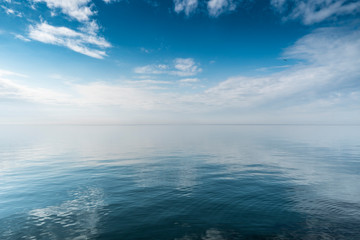 Fototapeta premium Beautiful white clouds on blue sky over calm sea with sunlight reflection, Harmony of calm water surface.