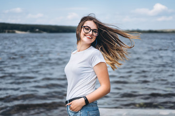 Portrait of a beautiful young woman in stylish glasses. Girl in white tshirt posing on the background of the lake landscape