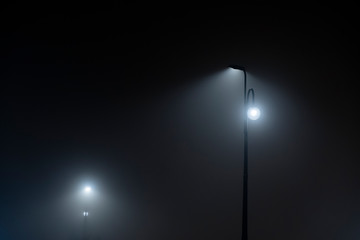 Fototapeta na wymiar Lamp post in fog. Street light's beam in foggy night. Dense fog.
