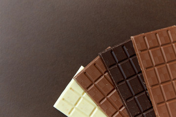 sweets, confectionery and food concept - milk, dark and white chocolate bars on brown background