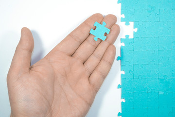 Woman's hand is holding a piece of puzzle. Hand assembling jigsaw puzzle.
