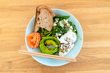 Healthy food. Salad with fish: salmon, yeast-free bread, poached egg, avocado, spinach, chio seeds, sesame seeds, pumpkin seeds, cottage cheese. Chopsticks. Wood background.