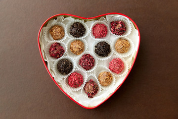 sweets, confectionery and food concept - candies in red heart shaped chocolate box on brown background
