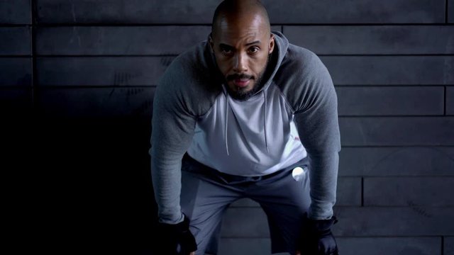 Serious determinate african american male runner in active wear resign after workout breathing deeply near mockup wall