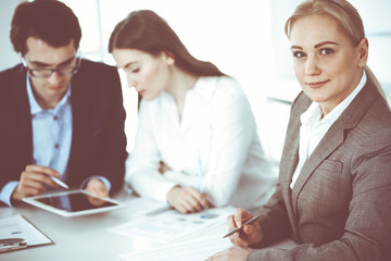 Fototapeta premium Headshot of business woman at negotiation. Group of business people discussing questions at meeting in modern office. Teamwork, partnership and business concept
