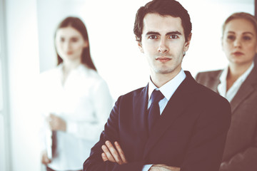 Headshot of businessman standing straight with colleagues at background in office. Group of business people discussing questions at conference or presentation. Success and business concept