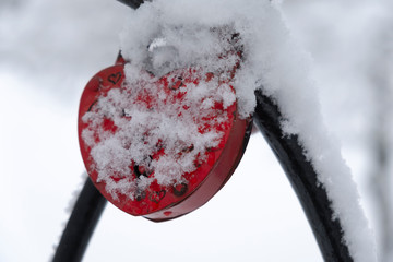 Heart locks covered with snow hanging on love bridge.