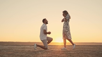 A young man is making a proposition to a nice blonde woman on the sunny beach near the lake