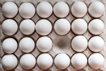 White chicken eggs in a cardboard box with one empty space, background.