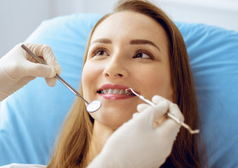 Smiling young woman with orthodontic brackets examined by dentist at dental clinic. Healthy teeth and medicine concept