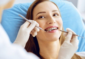 Smiling young woman with orthodontic brackets examined by dentist at dental clinic. Healthy teeth...