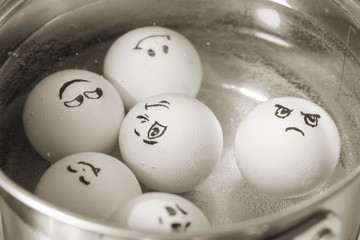White eggs in boiling in pot with different faces painted on them. Eggs with emotions.