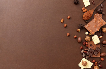 confectionery and food concept - milk, dark and white chocolate bars with nuts, candies, cocoa beans and powder on brown background