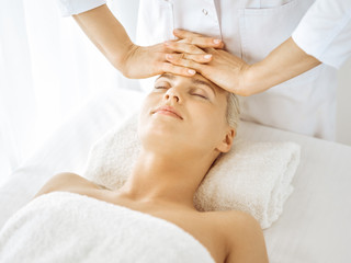 Fototapeta na wymiar Beautiful blonde woman enjoying facial massage with closed eyes. Relaxing treatment in medicine and spa center concepts
