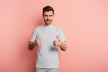 smiling handsome man showing thumbs up while looking at camera on pink background