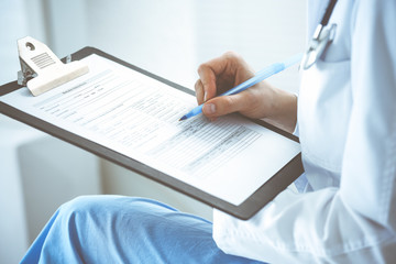 Woman doctor at work at hospital. Young female physician write prescription or filling up medical form while sitting in hospital office, close-up