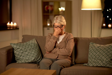old age, vision and people concept - tired senior woman in glasses rubbing her eyes at home at night