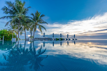 Beautiful poolside and sunset sky. Luxurious tropical beach landscape, deck chairs and loungers and water reflection over the swimming pool. Luxury summer vacation or holiday, hotel resort