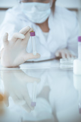 Close-up of professional female scientist in protective eyeglasses making experiment with reagents in laboratory. Medicine and research concept