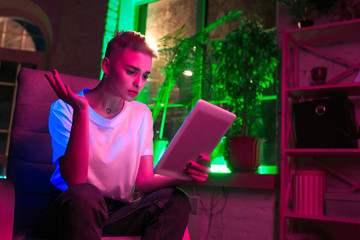Asking. Cinematic portrait of stylish woman in neon lighted interior. Toned like cinema effects, bright neoned colors. Caucasian model using tablet in colorful lights indoors. Youth culture.