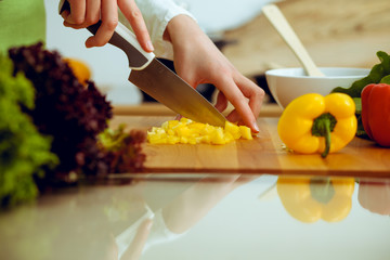 Obraz na płótnie Canvas Unknown human hands cooking in kitchen. Woman slicing yellow bell pepper. Healthy meal, and vegetarian food concept