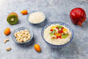 Bowl of rice flakes porridge with kiwi slices,pomegranate seeds,cumquats and cashew nuts on grey concrete background,top view