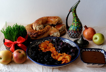 Traditional food of holiday Navruz: national dessert of Central Asia called Sumalak, lavash bread, assortment of dry fruits and fresh fruits – apples and pomegranate. Young green wheat with red ribbon
