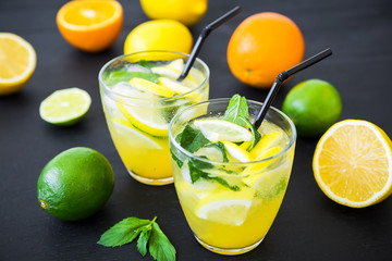 Citrus refreshing drink with limes and lemons in glasses. Ice lemonade on dark
