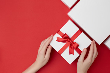 Women's hands holding white present box with red ribbon surrounded with white boxes on the red background