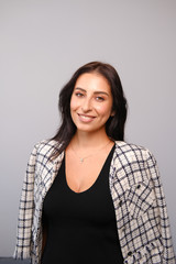 Fototapeta premium Portrait of a smiling mid-aged business woman with dark hair and brown eyes in glasses in jacket against a light wall