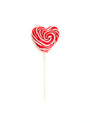 Sweet curled red and white heart-shaped lollipop on a wooden stick on a white isolated background. Love and feelings in candy.